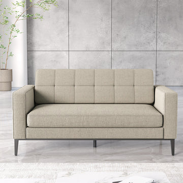 A modern two-seater sofa in light beige textured fabric with a tufted backrest and dark metal legs, set against a gray paneled wall and light marble floor.